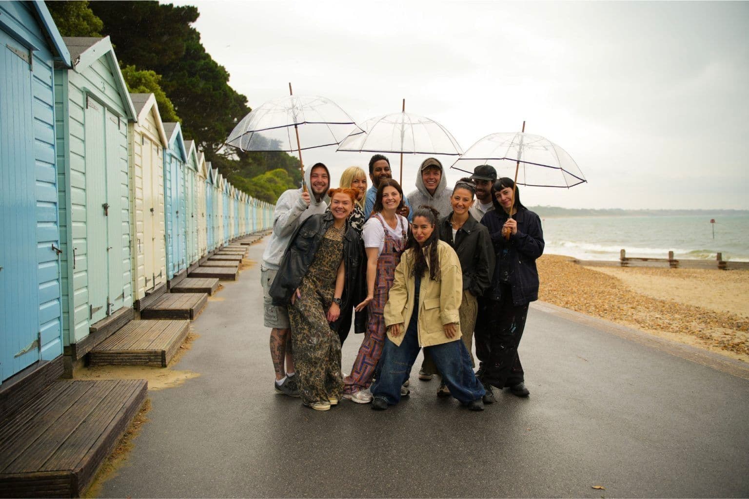 The ten designers of Interior Design Masters huddle together underneath umbrellas next to their beach huts.
