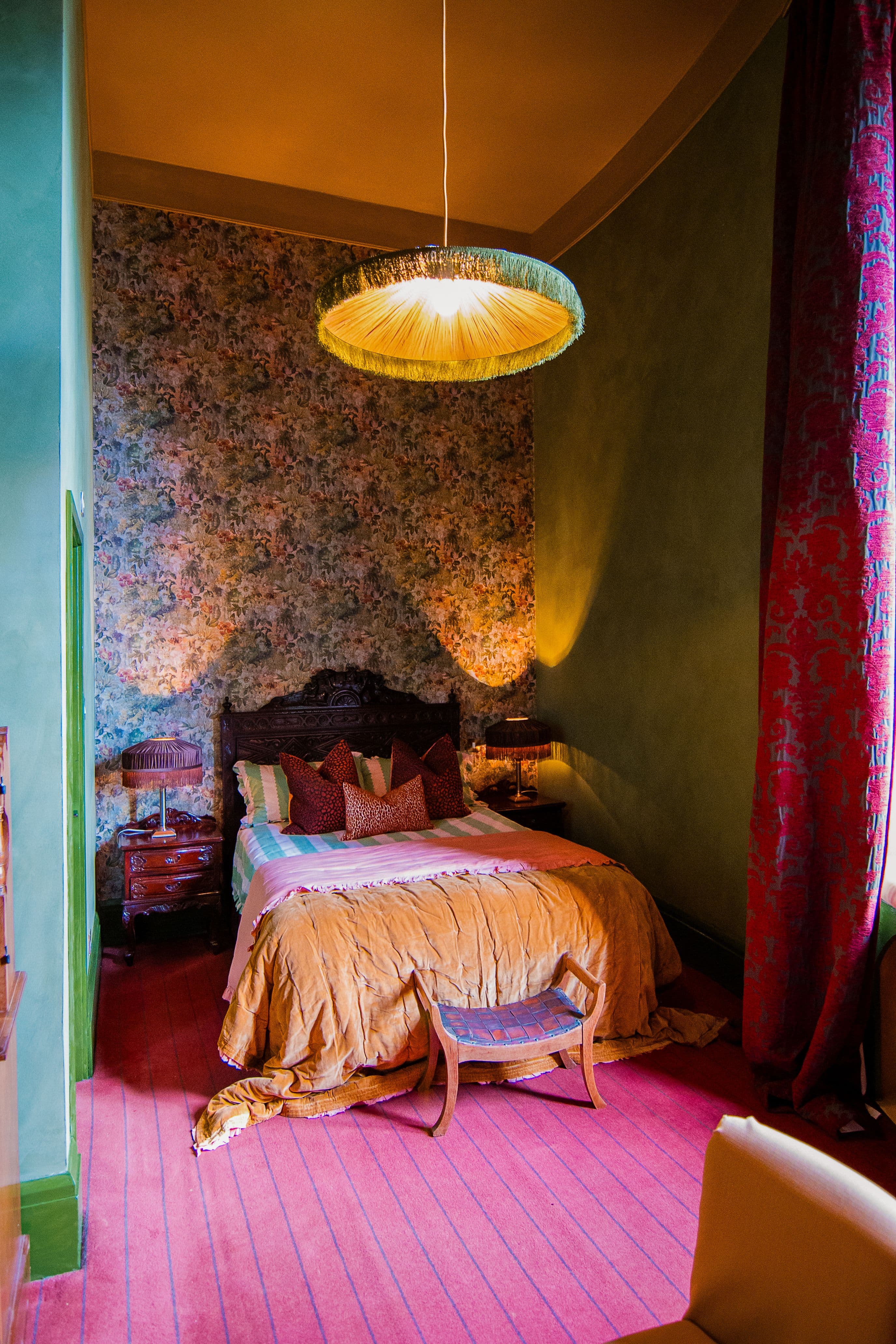 A beautifully designed hotel room at Peckforton Castle, complete with greens, reds and warm caramel colours, maximalist print and oversized fringed lightshade